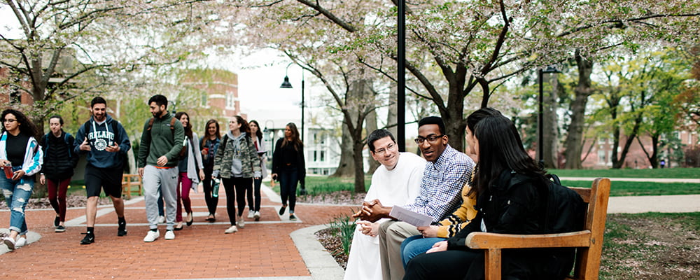 Friar sitting with students outside